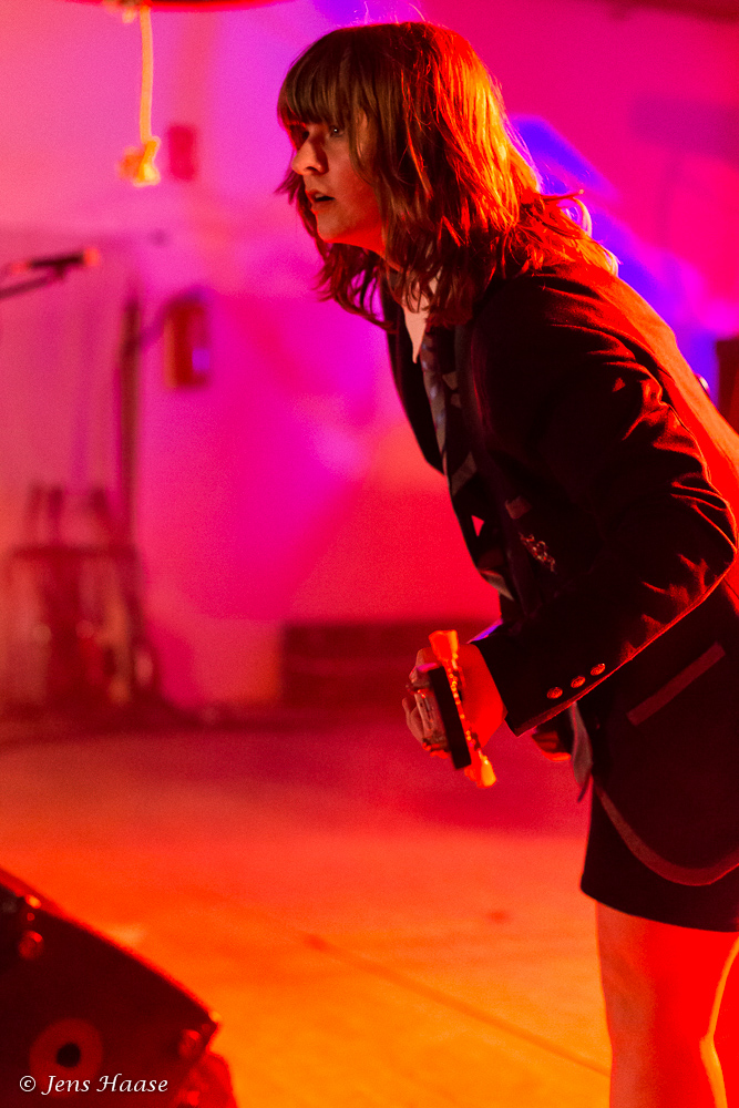 Weibliches Angus-Young-Double on stage, Interaktion mit Publikum, seitliche Perspektive, rosa Licht