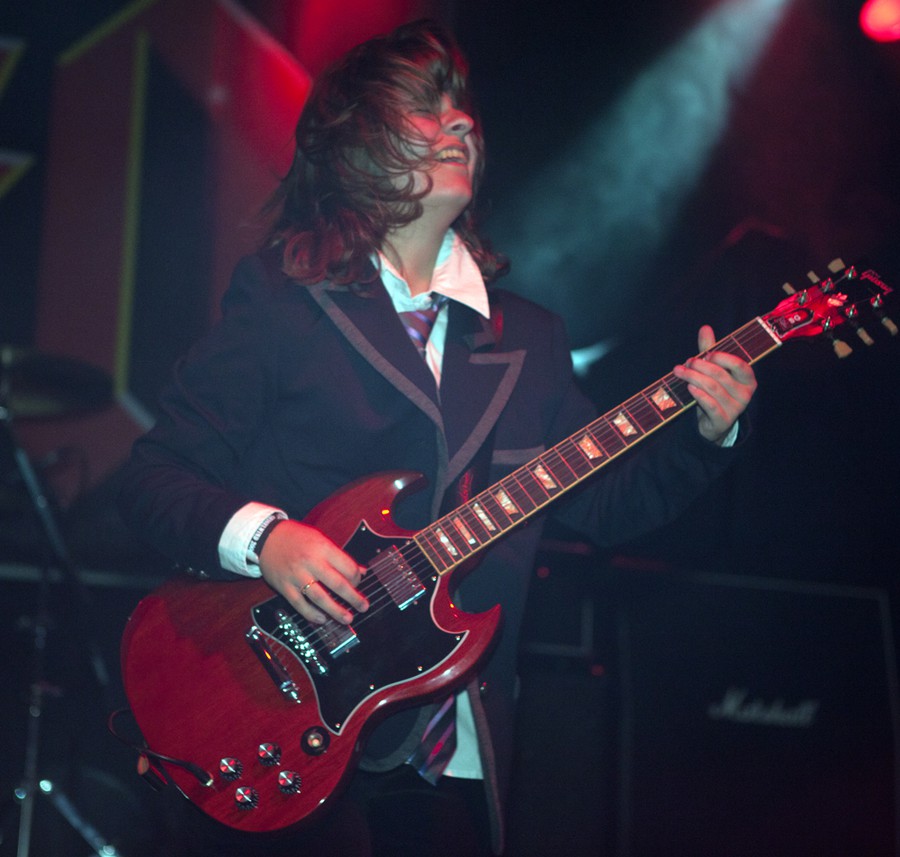 Weibliches Angus-Young-Double spielt auf der Bühne, in Aktion, fliegende Haare, rote E-Gitarre