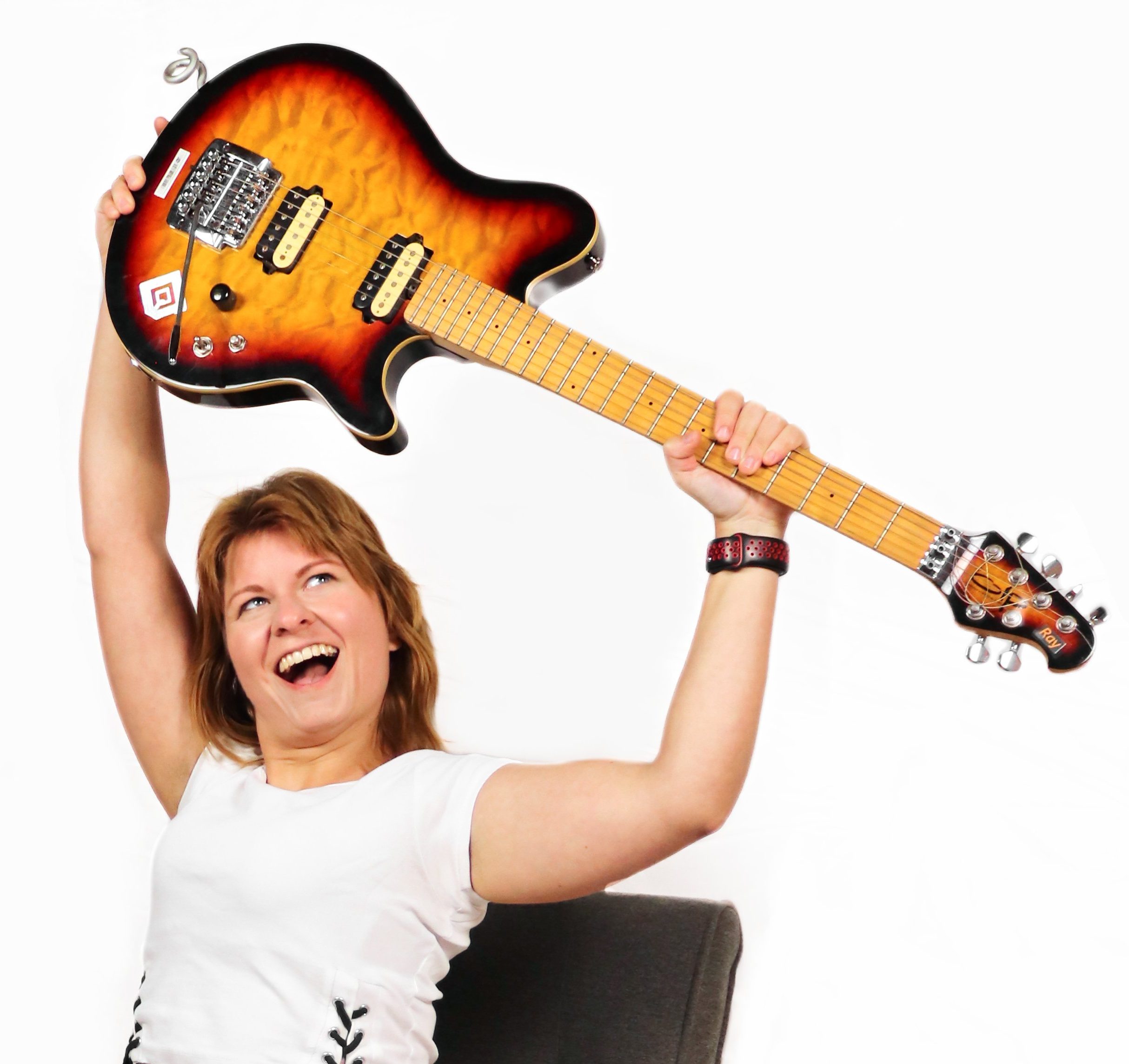 Frau mit weißem Shirt, die eine E-Gitarre in Sunburst Look mit energischer Pose nach oben hält